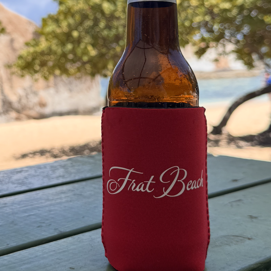Frat Beach coozie in red with white Frat Beach script, holding a bottle on a beach picnic table
